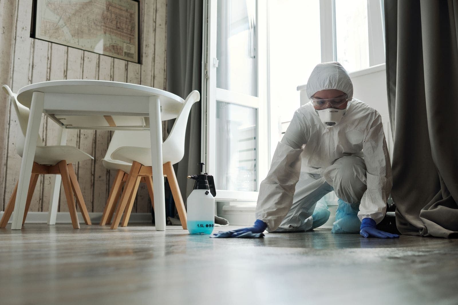 Technician in a protective suit and mask disinfecting a floor