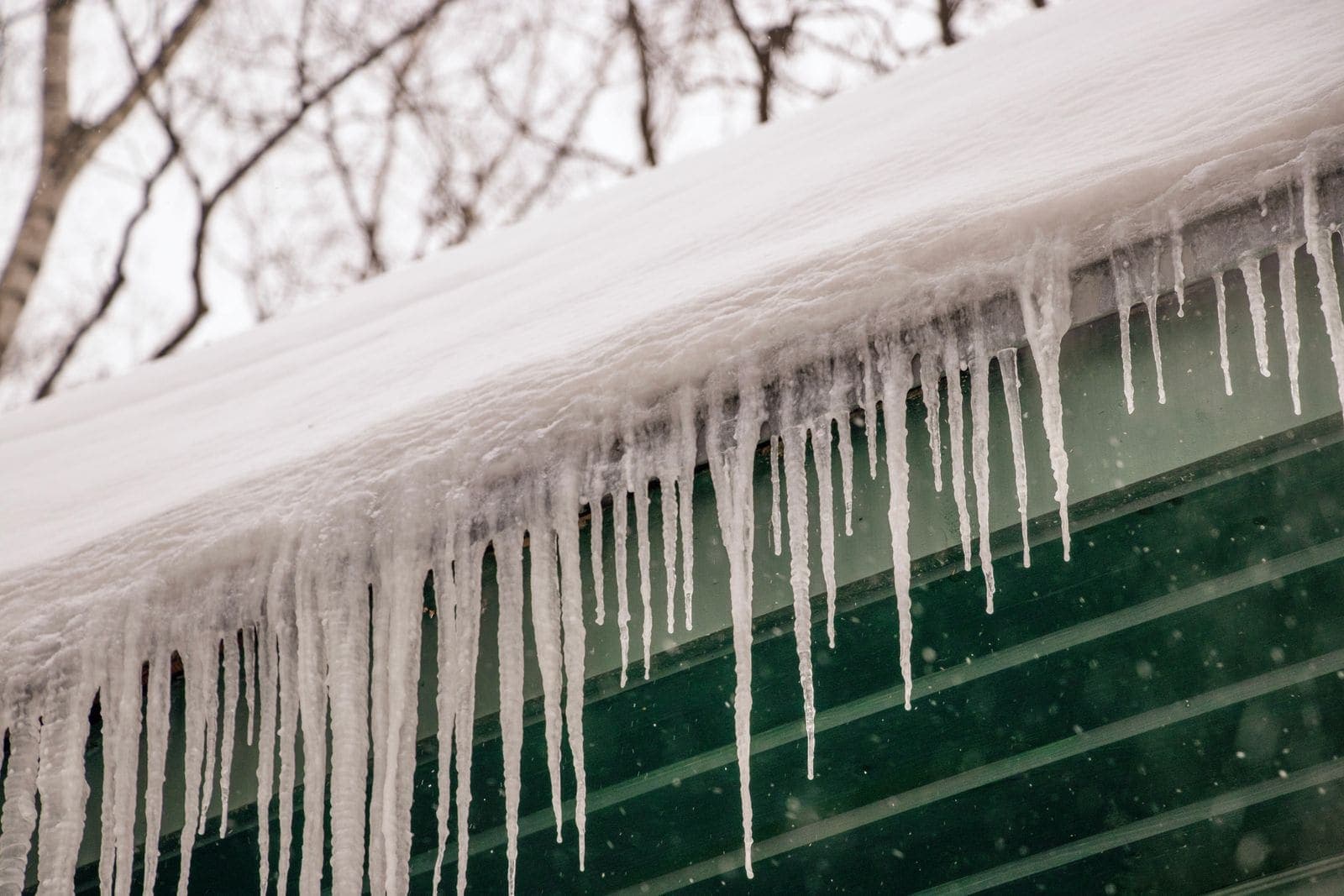 Icicles hanging from a snow-covered roof edge, a sign of ice dams